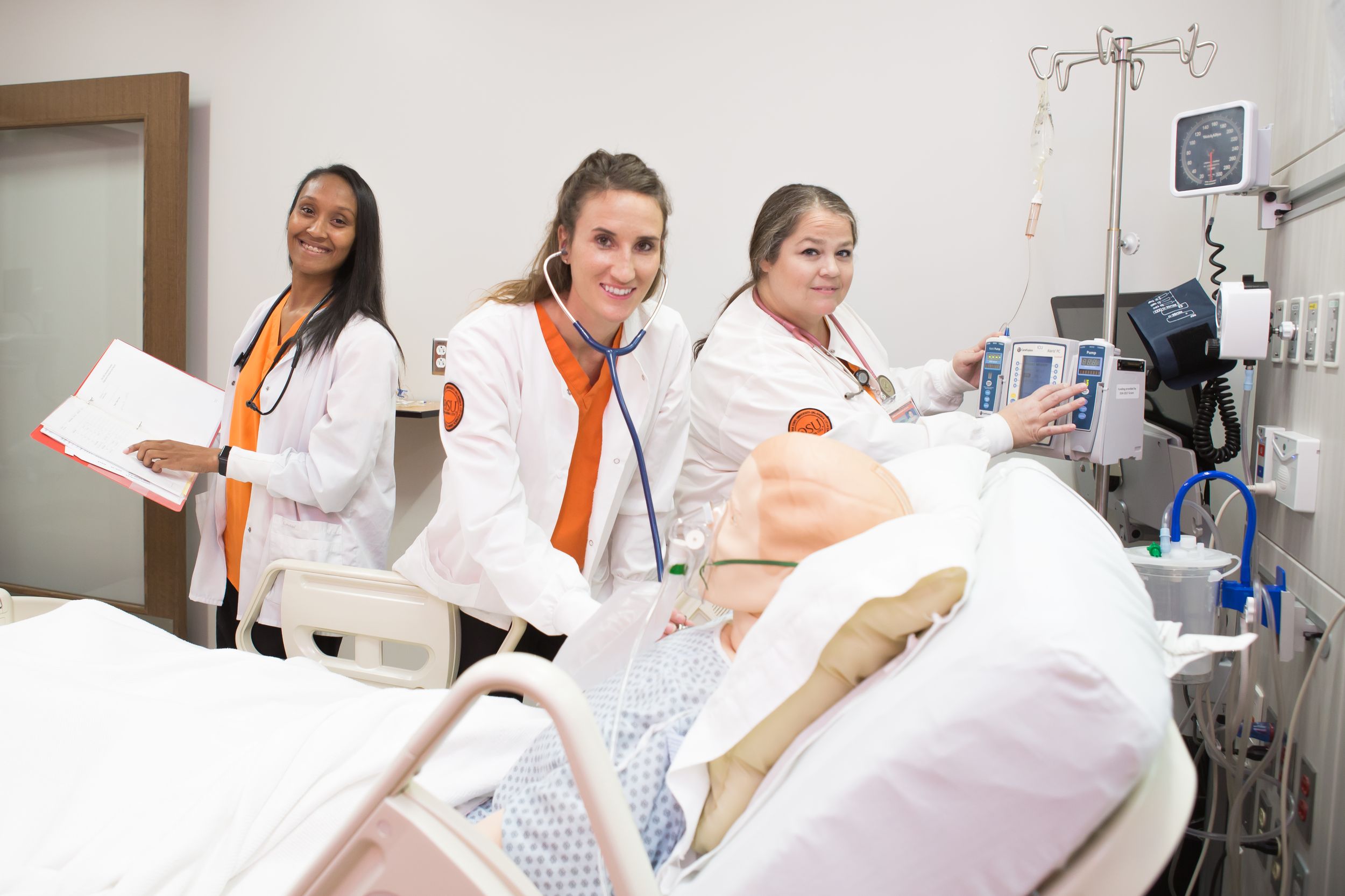 3 nursing students work on a medical manikin in a hospital bed