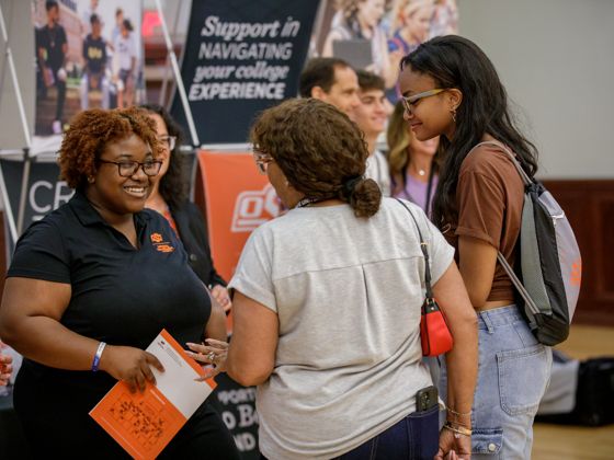 Student representative smiling and speaking to new students during Orientation and Enrollment browse sessions.