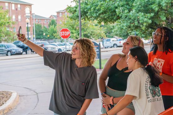 4 girls post for a selfie as the one in the front takes it.